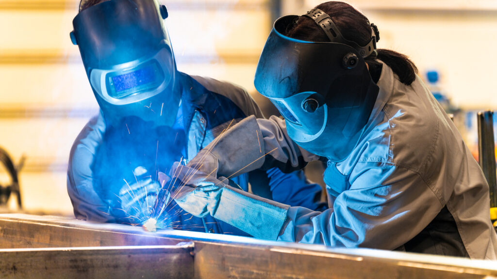 Alt text: Two welders work together on a sheet metal project.