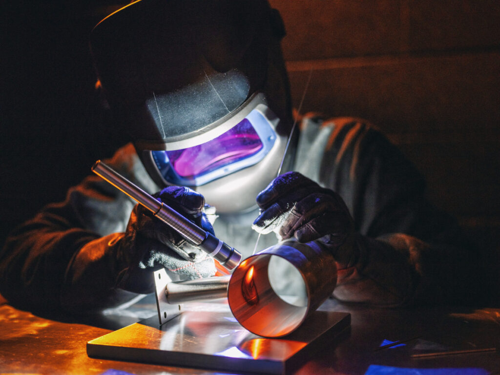 A close-up photo of a welder performing TIG welding on sheet metal.