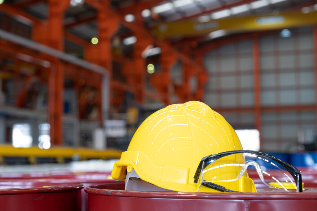 A yellow hard hat rests in the foreground of a photo taken in a facility that utilizes machine guarding for worker safety.
