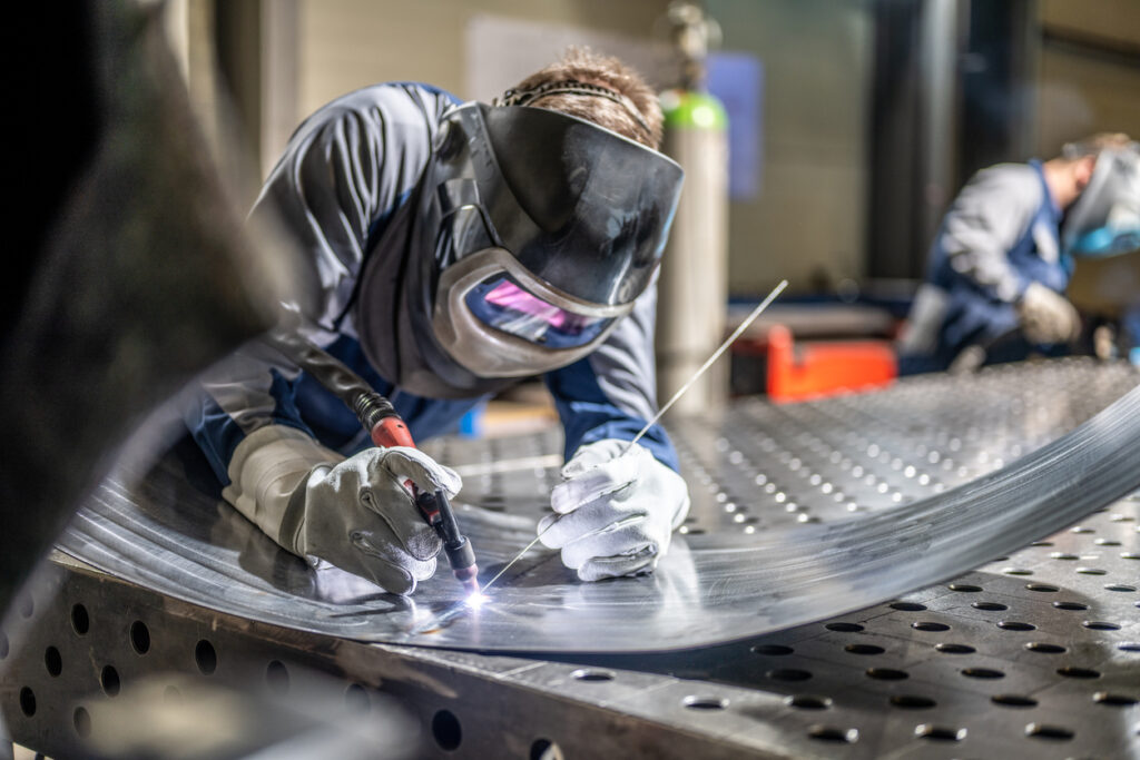 Alt text: A welder wears a mask as they work with sheet metal.