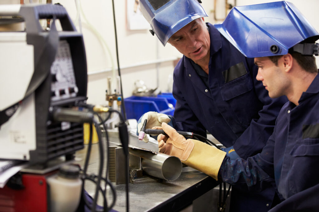 Alt text: A welder tech listens to his instructor as he works toward his certification.
