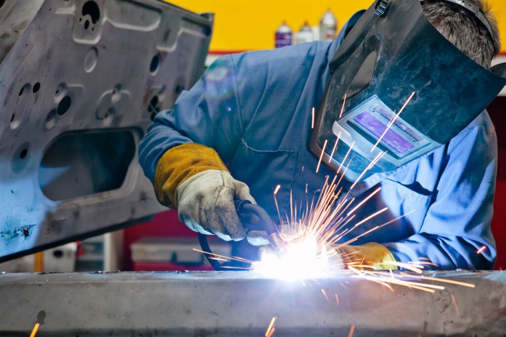 A masked welder sends sparks flying as he works on a welding project.